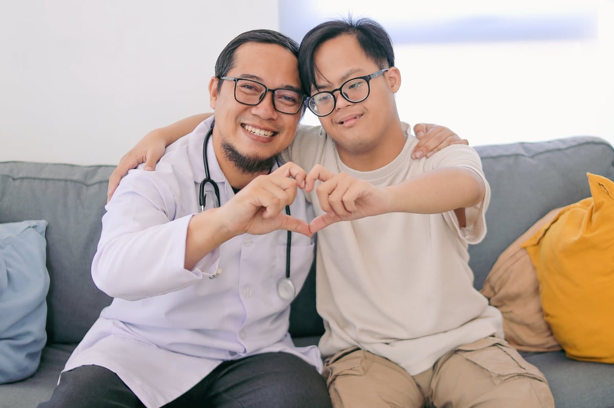 A happy man with Down syndrome and a caregiver making a heart shape together
